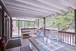 Une terrasse extérieure couverte, équipée d’un barbecue, de sièges et d’une nappe à carreaux.