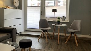 Un salon moderne comprenant un canapé, deux fauteuils, une petite table, une lampe, une plante en pot et une fenêtre avec des stores.