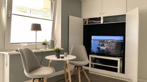 Un espace de vie compact comprenant un téléviseur, deux fauteuils, une petite table et une fenêtre.