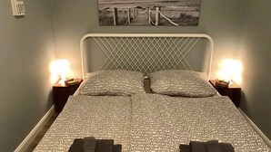 Un lit bien fait, avec une literie à motifs, deux lampes de chevet et un tableau encadré au mur.