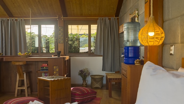 Una habitación acogedora con techo de madera, cama con ropa de cama blanca, escritorio con silla y un dispensador de agua grande.