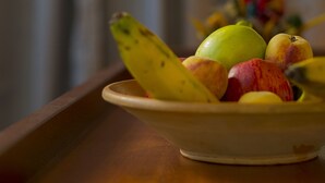 Un frutero con fruta sobre una mesa de madera, fondo desenfocado.