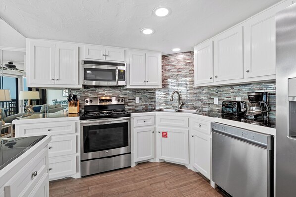 A modern kitchen with white cabinetry, stainless steel appliances, and a mosaic backsplash. - Sandpiper Condominiums 403, Panoramic Gulf Views w/ direct access to Mustang Island/Port A beaches. (Port Aransas)