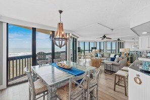 A spacious living area with a large dining table, comfortable seating, and a view of the ocean. - Sandpiper Condominiums 403, Panoramic Gulf Views w/ direct access to Mustang Island/Port A beaches. (Port Aransas)