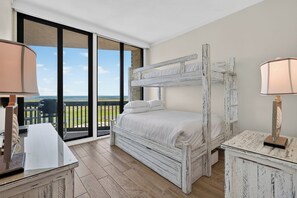 Ein Etagenbett mit weißer, abgenutzter Optik, ein Schreibtisch mit Lampe und Blick ins Freie durch große Schiebetüren.