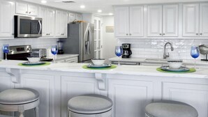 A modern kitchen with white cabinetry, stainless steel appliances, and a central island with stools.