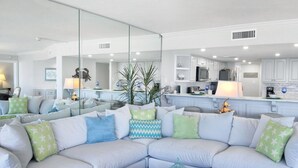 A modern living room with a light-colored sectional sofa, a round coffee table, and a kitchen in the background.