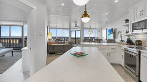 A spacious kitchen with white cabinetry, a marble island, and a large window overlooking a deck.