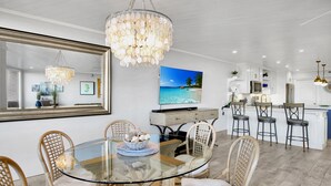 A modern kitchen with white cabinetry, a large island with bar stools, and a television displaying a tropical beach scene.