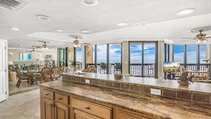 A spacious kitchen with a large island, wooden cabinets, and a view of the ocean through large windows. - Sandpiper Condominiums 903L, Panoramic Gulf Views w/ direct access to Mustang Island/Port A beaches. (Port Aransas)