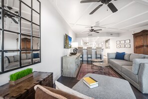 A spacious living area with a gray sofa, a coffee table, and a bookshelf. There is a dining area with a table and chairs in the background.