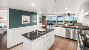 A modern kitchen with white cabinetry, a black countertop, and a view of the outdoors through large windows.
