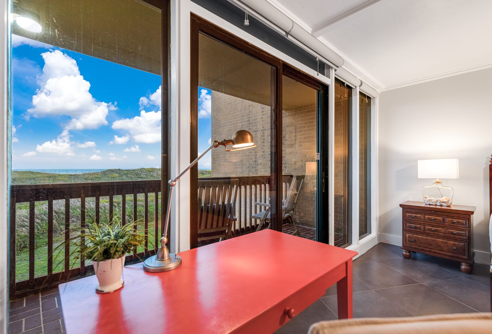 Un balcone con un tavolo rosso, una lampada e una pianta in vaso.