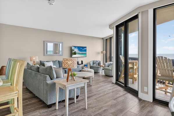 A modern living room with a grey sofa, a coffee table, and a view of the sea through large windows.