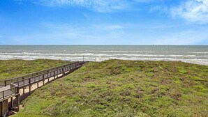 Une vue sur la côte, avec une promenade en bois menant à la plage, un terrain herbeux et un ciel dégagé.