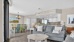 Un salon spacieux avec un canapé gris, une table basse en bois et un coin repas agrémenté de chaises colorées.