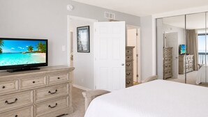 A bedroom with a bed, a dresser, a television, a door, and a mirror.
