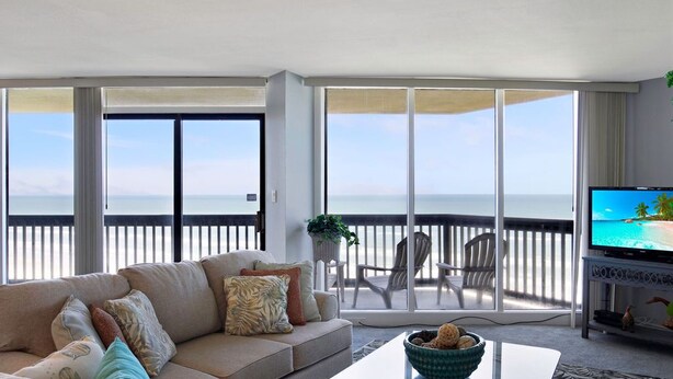 Un salon avec un canapé, une table basse et un téléviseur. Il y a un balcon avec vue sur l’océan.