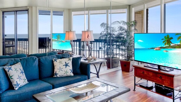 Un salón amplio con televisor grande, asientos cómodos y un balcón con vistas al océano.