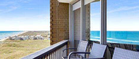 A balcony with wicker chairs overlooking a beach and ocean view.