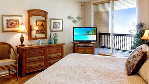 Un dormitorio con una cama grande, televisión, cómoda y una silla. Cuenta con un balcón con vista al océano.