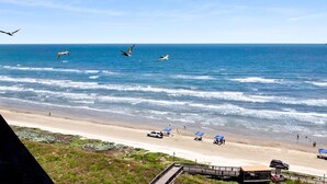 Una playa con olas, una carretera y algunos vehículos.