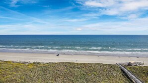 Une plage avec une promenade en bois menant à une construction, d’où l’on a une vue sur l’océan.