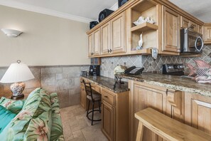 A compact kitchen with wooden cabinets, a granite countertop, and a built-in microwave.