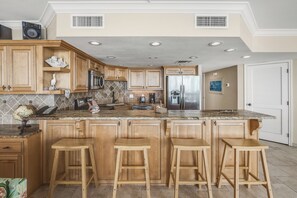 A modern kitchen with wooden cabinets, a granite countertop, stainless steel appliances, and a central island with bar stools.