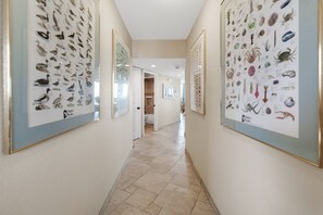 Een gang met ingelijste illustraties van dieren in de wildernis aan de wanden, die leidt naar een badkamer met een bad en douche.