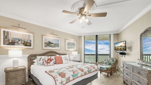 Un dormitorio con una cama grande, ventilador de techo, televisor y vistas al exterior por la ventana.