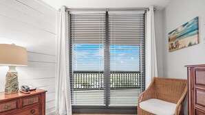 Une pièce avec une porte-fenêtre coulissante, une chaise en osier, une commode en bois et un tableau accroché au mur.