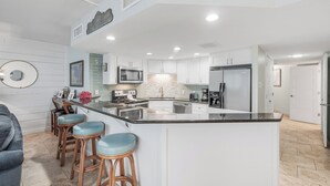 Une cuisine moderne avec des meubles blancs, un îlot central doté de tabourets, des appareils en acier inoxydable et un dosseret de carrelage disposé en motif chevrons.