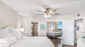 Une chambre avec un grand lit, un ventilateur de plafond et une vue sur un balcon par une porte ouverte.