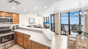 Une cuisine moderne avec des meubles en bois, un grand îlot central et une vue sur un balcon aménagé avec du mobilier d’extérieur.