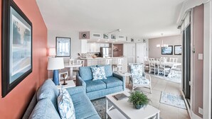 Un salon moderne avec un canapé bleu, un coin repas avec des chaises blanches et une cuisine en arrière-plan.