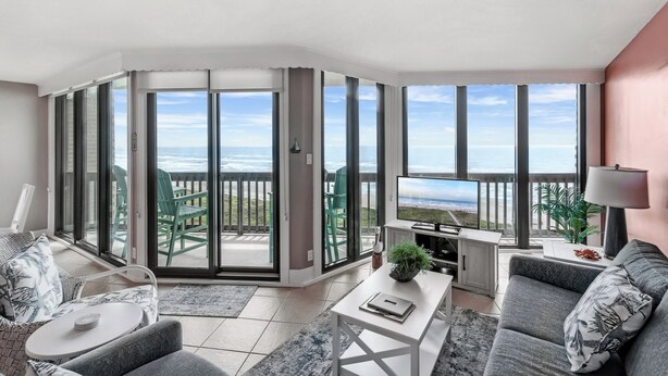 Un salon moderne doté d’une grande porte-fenêtre coulissante donnant sur un balcon avec vue sur l’océan.