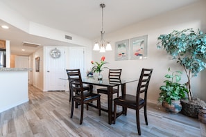 A dining area with a glass table, wooden chairs, a chandelier, and potted plants.