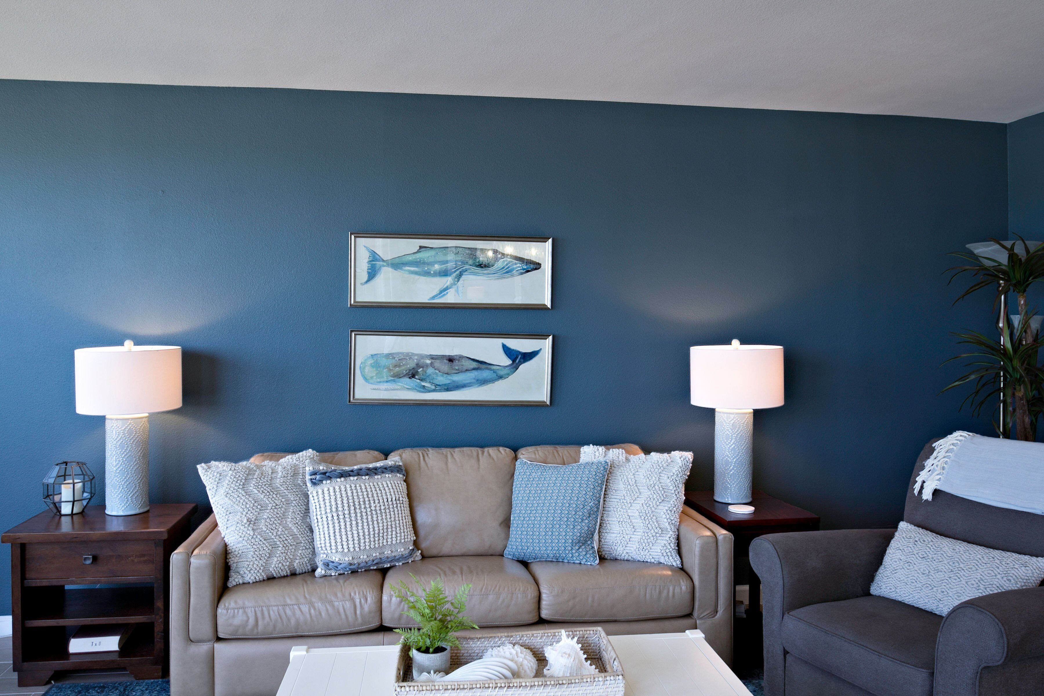 A living room with a beige sofa, two wall-mounted lamps, and two framed whale paintings.