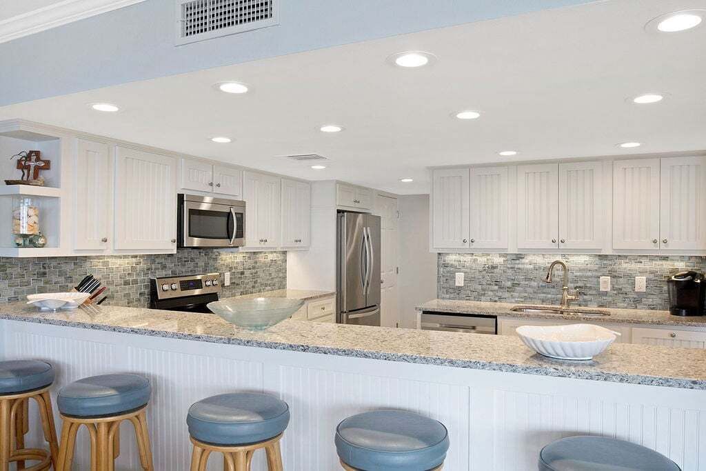A modern kitchen with white cabinetry, stainless steel appliances, a large island with stools, and a tiled backsplash.