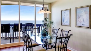 A dining area with a glass table and chairs, a hanging light fixture, and two framed artworks on the wall. - Sandpiper  #1007: Beachfront 2 Bedroom 2 Bathroom With Spectacular Views and 24 Hour Management (Port Aransas)