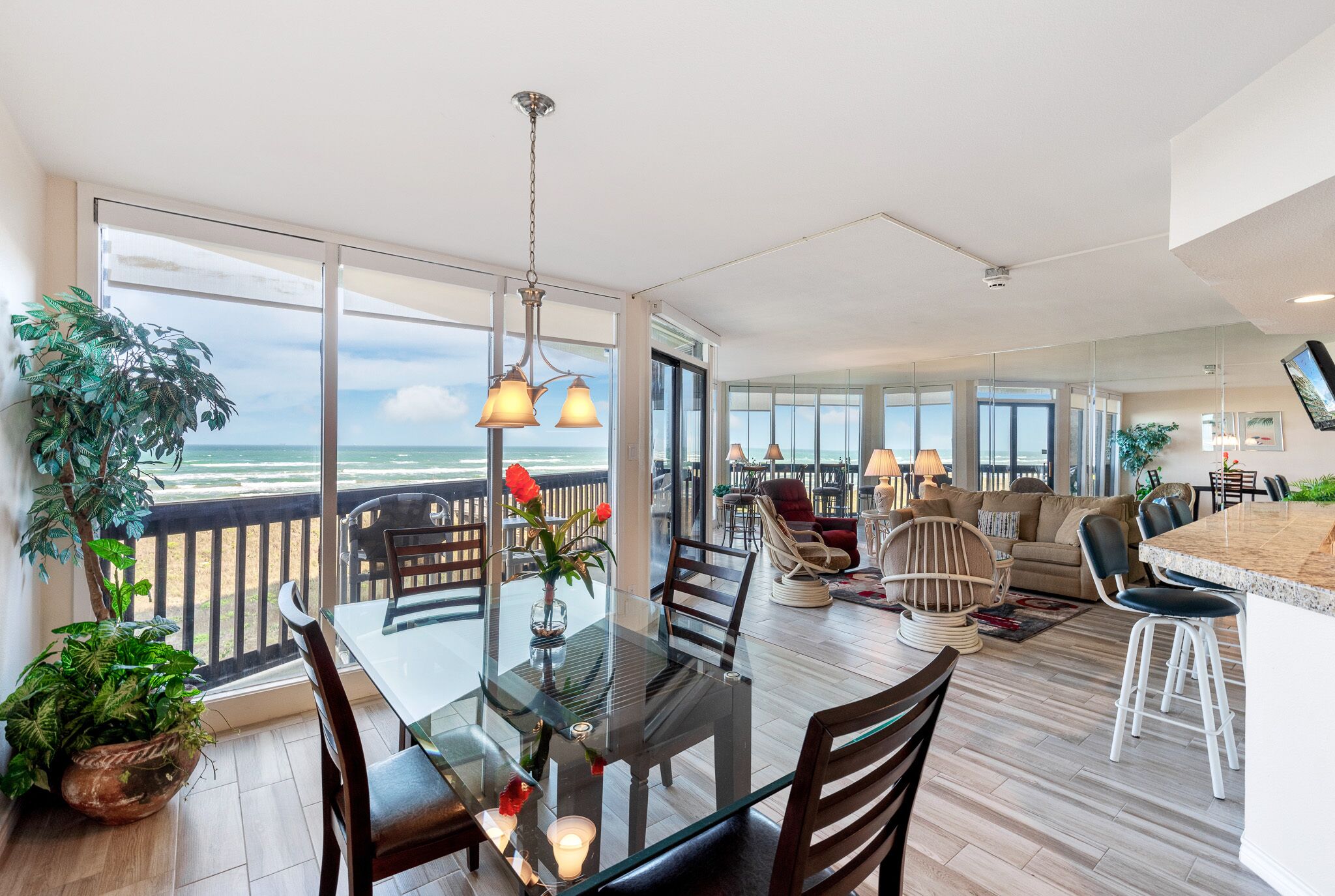 Un vaste espace de vie doté d’une grande porte vitrée donnant sur un balcon avec vue sur l’océan, et aménagé avec une table à manger, des chaises et un canapé.