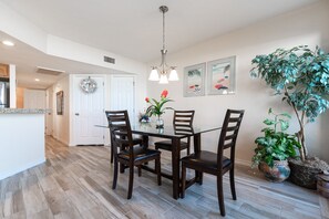 A dining area with a glass table, wooden chairs, a chandelier, and potted plants.