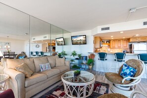 Un salon moderne avec un canapé beige, une table basse en verre et un fauteuil en osier.