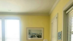 Una stanza con due poltrone blu, un poggiapiedi fantasia, un tavolino rotondo con una lampada e un quadro appeso al muro.