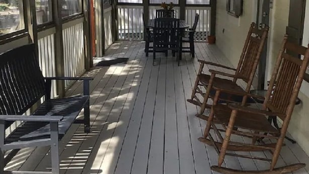 Un portico coperto con tavolo e sedie, poltrone a dondolo in legno e una panca.