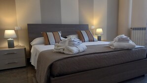 Ein ordentlich gemachtes Bett mit Kissen, ein Nachttisch mit Lampe und ein Heizkörper im Hintergrund.