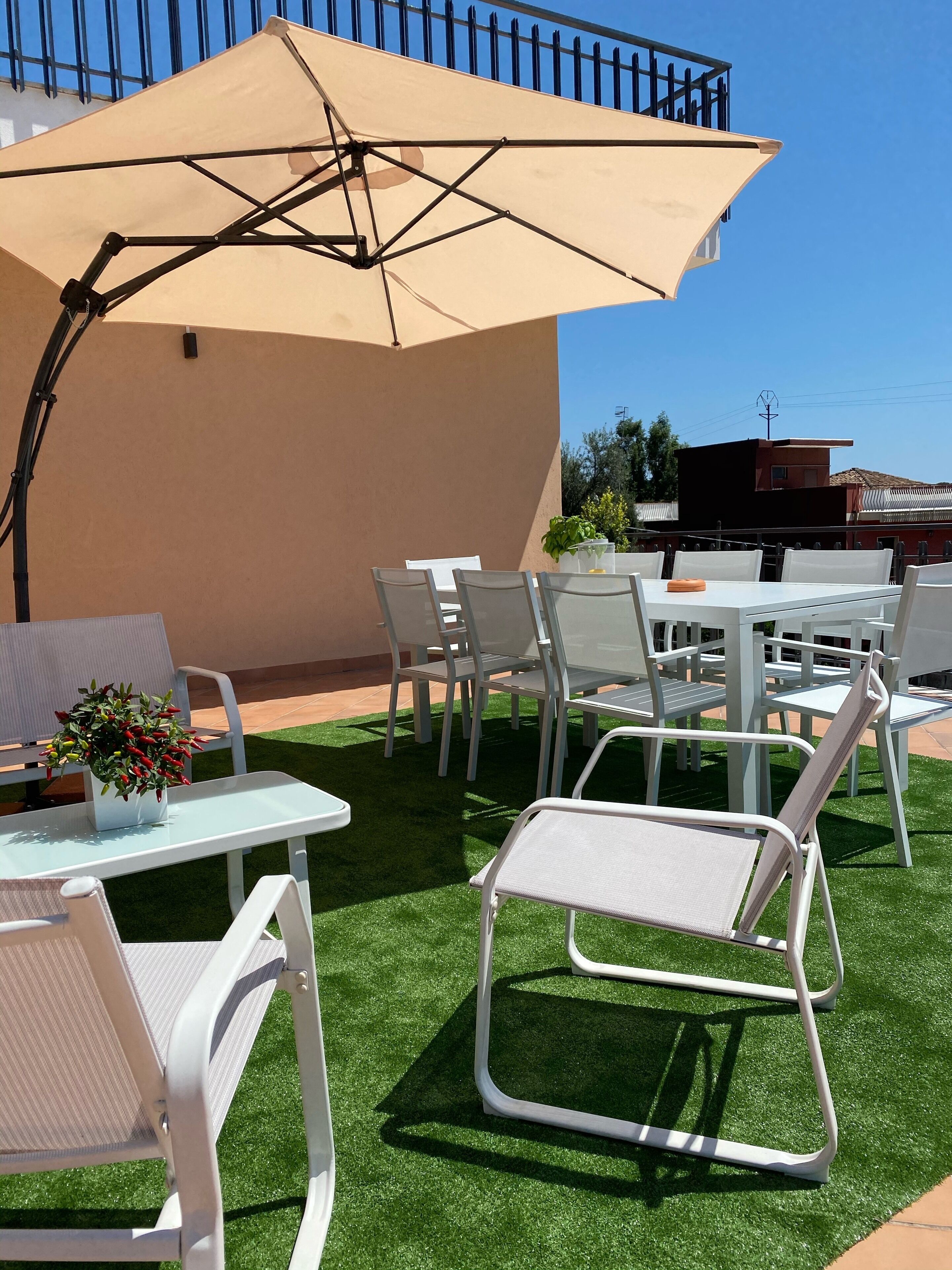 An outdoor patio with white metal chairs and tables, a beige umbrella, and artificial green turf.