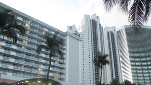 Un hotel moderno de gran altura con múltiples balcones, palmeras y un diseño arquitectónico contemporáneo.
