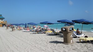 Una playa con tumbonas y sombrillas, una torre de salvavidas y cielos azules y despejados.